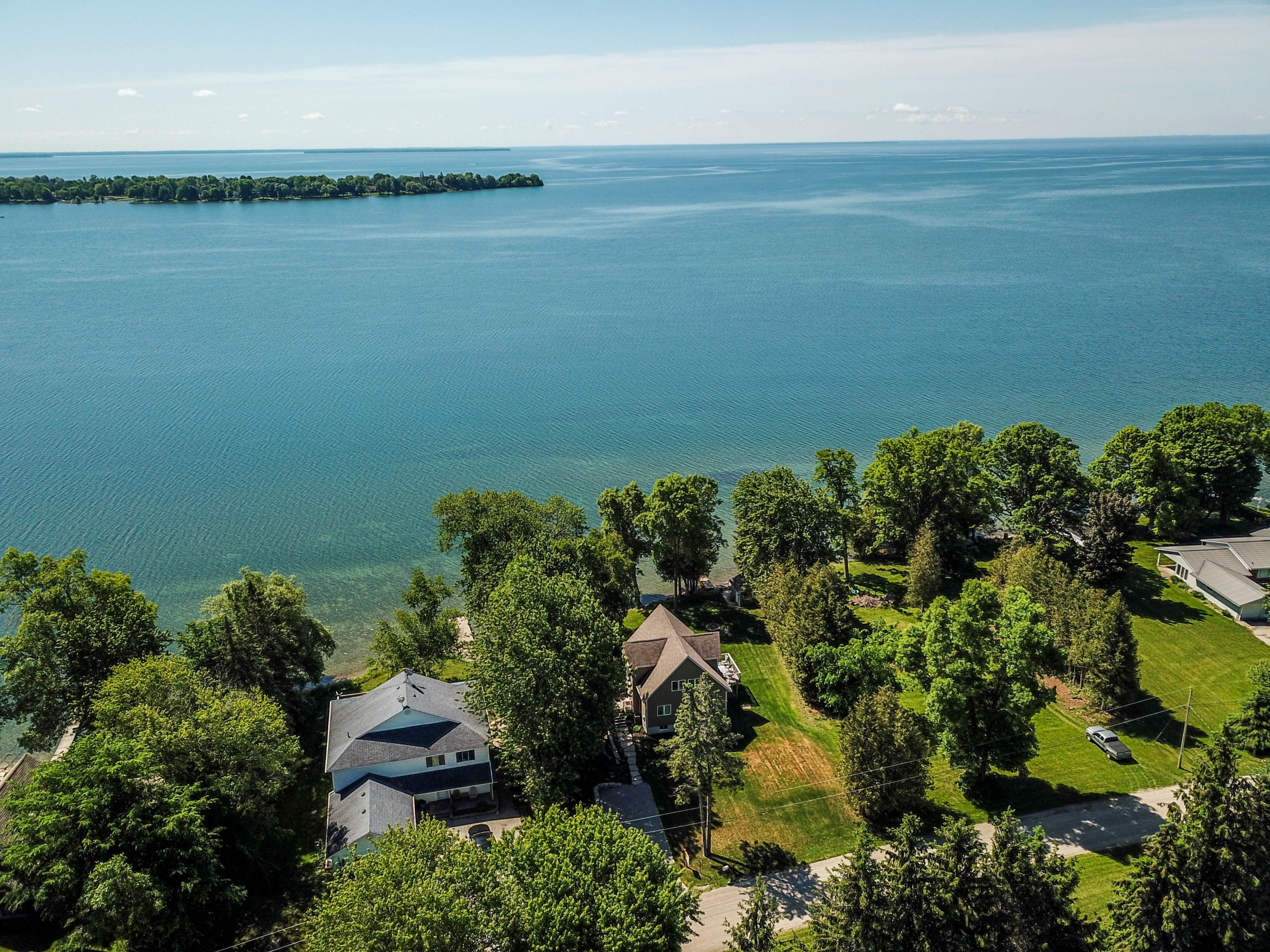 Aerial view over Lake Simcoe showing a treed shoreline and turquoise shallows, Ramara, Ontario