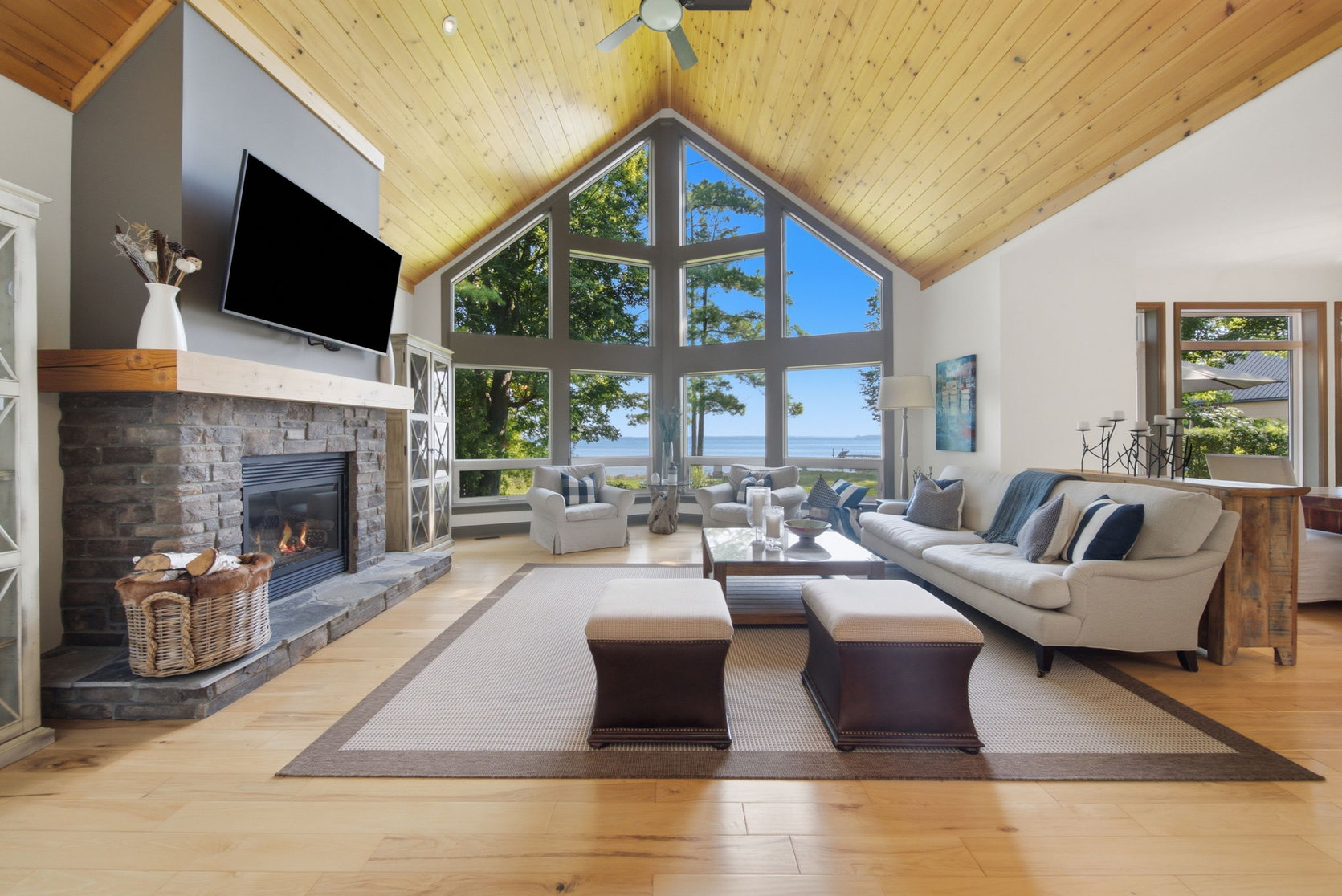Great room at 797 Woodland Drive with vaulted pine ceiling, stone gas fireplace and a two-storey window wall facing Lake Simcoe